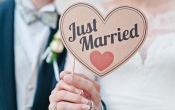 Closeup of newlyweds hands holding a sign saying Just Married, selective focus