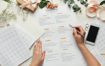 Wedding background with checklist and calendar. Female hands arranging marriage, filling in planners on white wooden table with lots of tender bridal stuff, top view